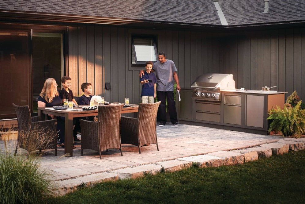 A family enjoying a meal outdoors next to the Napoleon Grills Built-In 500 Series 32-Inch 4-Burner Gas Grill Head integrated into a modern outdoor kitchen setup.