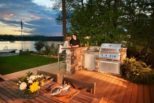  A lifestyle image of people enjoying an outdoor meal by the lake with the Napoleon Grills Built-In 700 Series 32-Inch Gas Grill Head as the focal point of their gathering.