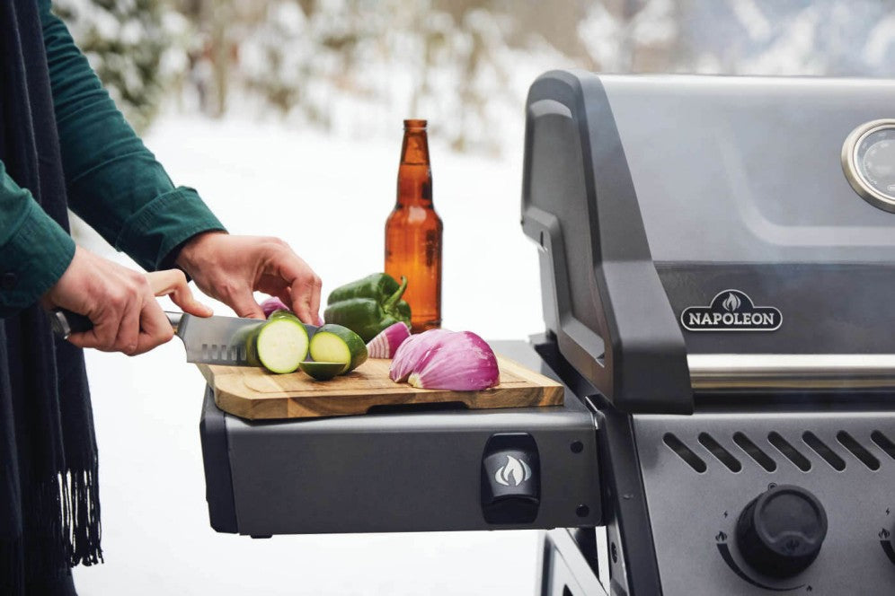 A person prepping food on a cutting board next to Napoleon Grills Freestyle 365 on a snowy day.