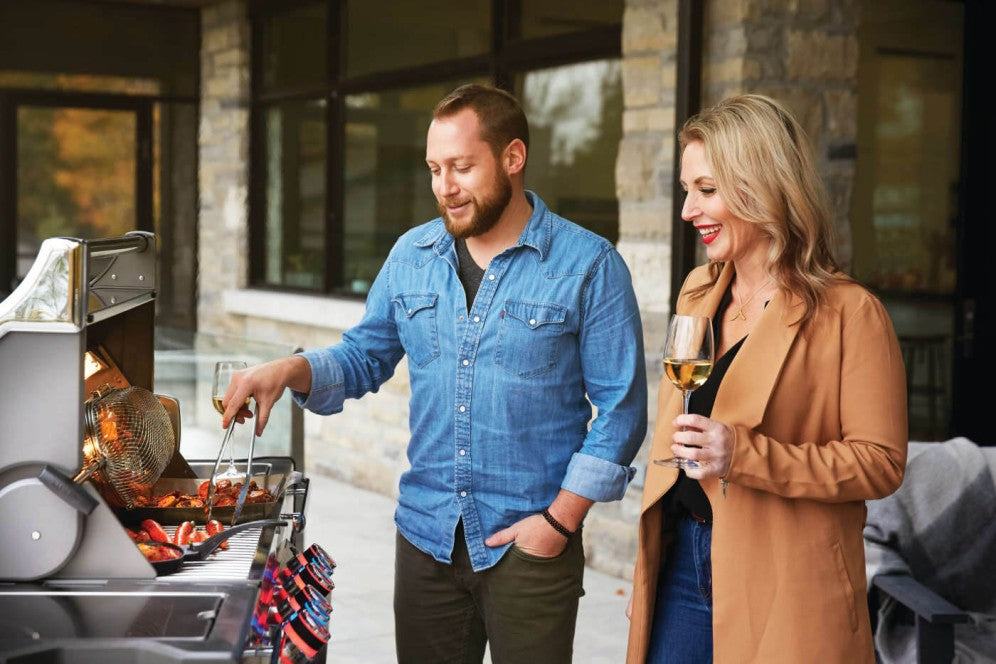 A man and woman enjoying a grilling session on the Napoleon Grills Prestige PRO™ 500 RSIB, featuring the grill's spacious cooking area and convenient side shelves.