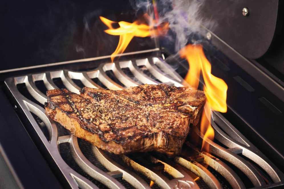 Close-up of a sizzling steak with grill marks on the cooking grates of the Napoleon Grills Phantom Prestige 500 RSIB, flames visible.