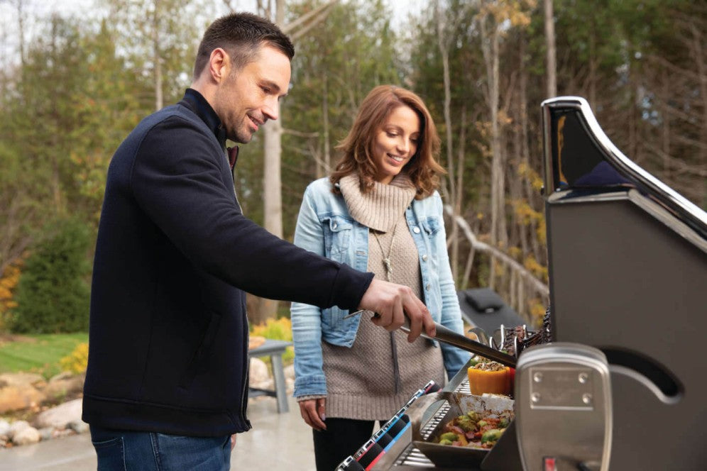 A man and woman grilling food on a Napoleon Grills Prestige PRO™ 665 RSIB, showcasing the grill's spacious cooking area.