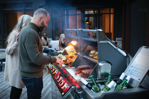 Lifestyle image of a couple grilling on the Napoleon Grills Prestige PRO™ 825 RSIB on a wooden deck at dusk.