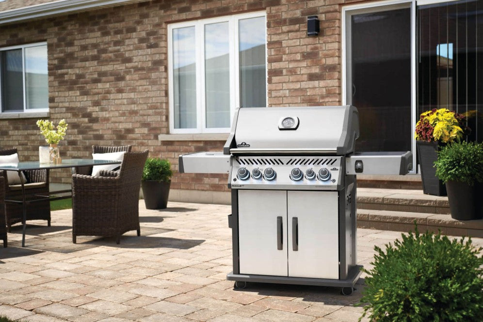 The Napoleon Grills Rogue SE 525 RSIB Grill placed on a patio in a backyard setting, featuring outdoor furniture and plants.