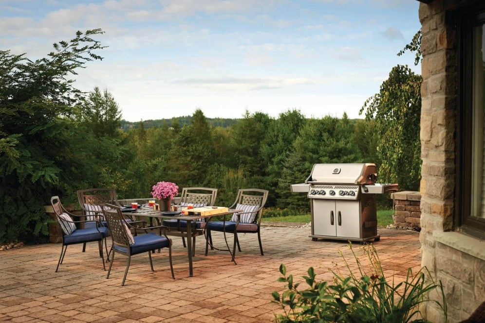 The Napoleon Grills Rogue SE 625 RSIB Grill set on a brick patio with outdoor dining furniture in a serene backyard.