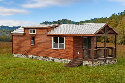 Pocono Cabin by Oasis Tiny Estates in the middle of a greenfield overviewing mountains and a blue sky.