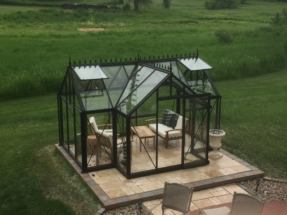 Exaco Orangerie Greenhouse by Janssens overlooking a pastoral rural landscape, featuring comfortable outdoor furniture on a stone patio.