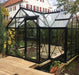 Janssens Exaco Orangerie Greenhouse with traditional black frame and clear panes, built on a wooden deck next to a pond in a residential backyard.