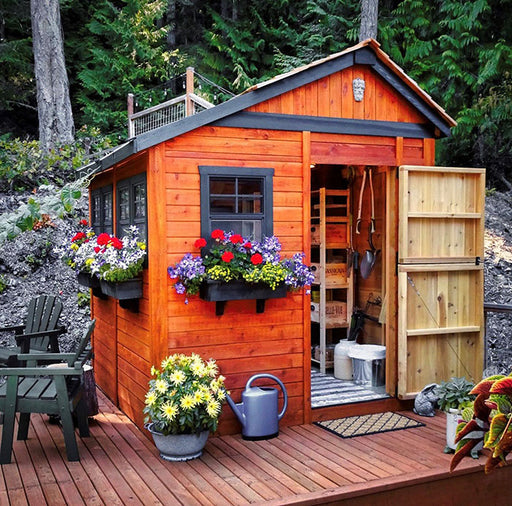 Warm cedar Outdoor Living Today Sunshed Garden Shed 8x8 adorned with vibrant flower boxes and welcoming open door on a forest backdrop.