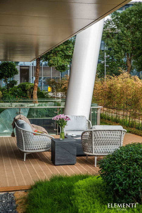 Elementi Colorado Series slate black side table placed in an outdoor lounge setting with wicker furniture and lush greenery.