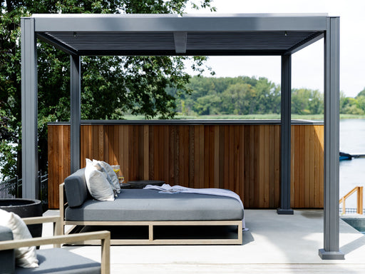  The Vikos Aluminum Stand Alone Pergola situated on a deck by a body of water, offering a covered outdoor area. The structure creates a contemporary and inviting space with the outdoor couch placed under it, accentuating the blend of comfort and style.