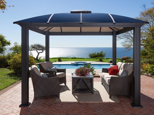 A luxurious black hard top gazebo with comfortable seating and a coffee table, overlooking a tranquil pool and the expansive sea horizon.