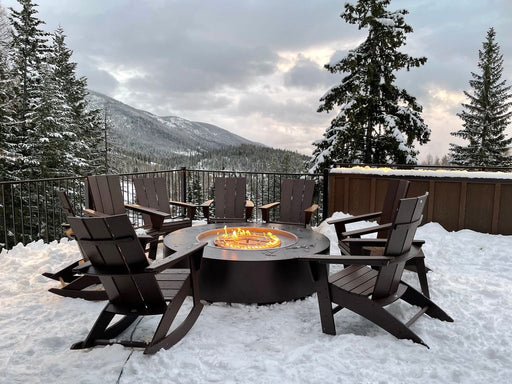 Round Unity fire pit by The Outdoor Plus, in a pewter powder-coated steel finish, offering warmth and elegance to a snowy mountain backdrop