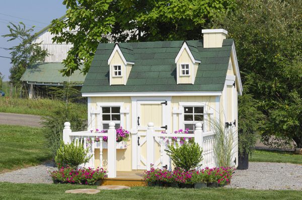 The Cape Cod Playhouse by Little Cottage Company with a green roof and white picket fence, nestled in a serene outdoor landscape.