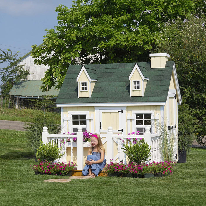 The Cape Cod Playhouse by Little Cottage Company with a green roof and white picket fence, nestled in a serene outdoor landscape.