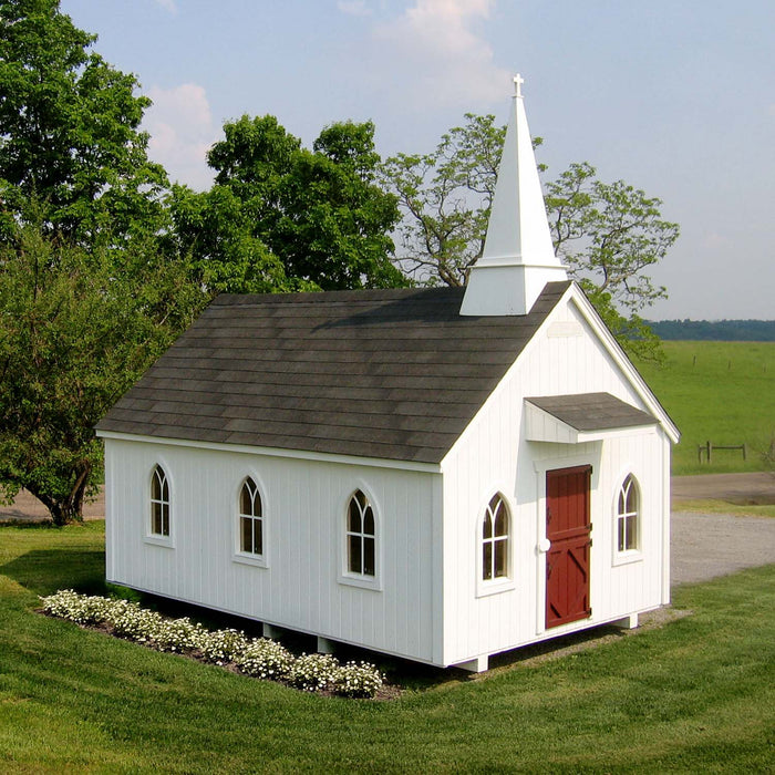 The Little Cottage Company's Chapel Playhouse in a meadow, as a traditional horse-drawn carriage passes by on a sunny day.