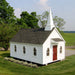 The Little Cottage Company's Chapel Playhouse in a meadow, as a traditional horse-drawn carriage passes by on a sunny day.