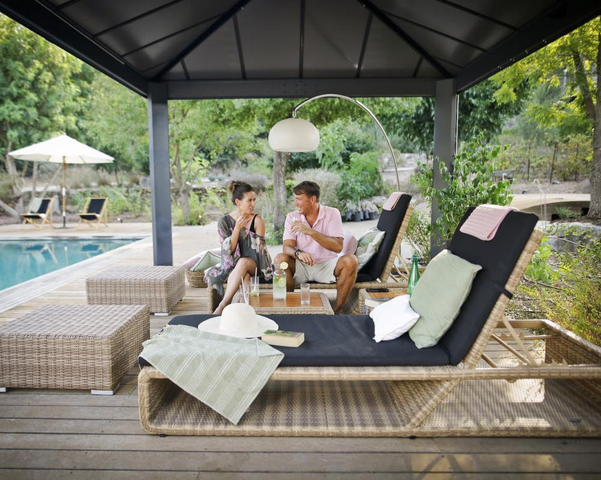 A couple talking in poolside while sitting on lounge chairs under a large Canopia Dallas Gazebo