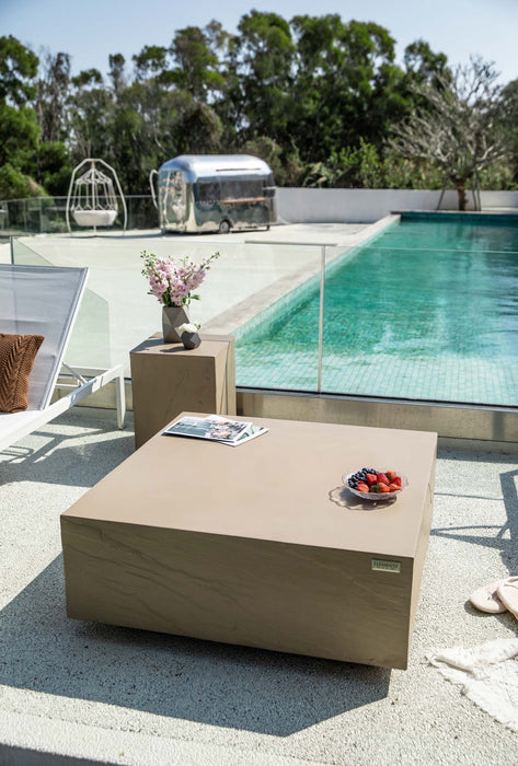 The sunlight yellow square medium Colorado coffee table from Elementi placed in a stylish poolside setting with modern decor and lush greenery.