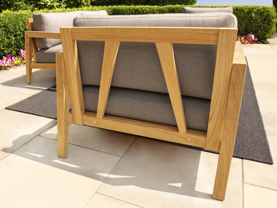  Profile view of Rhodes Chat Chair with wooden frame and cast slate cushions on a garden setting.