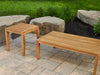 Close-up of the Rhodes Chat Set's wooden coffee table and side table without cushions, displayed on a stone-paved patio with natural landscaping.