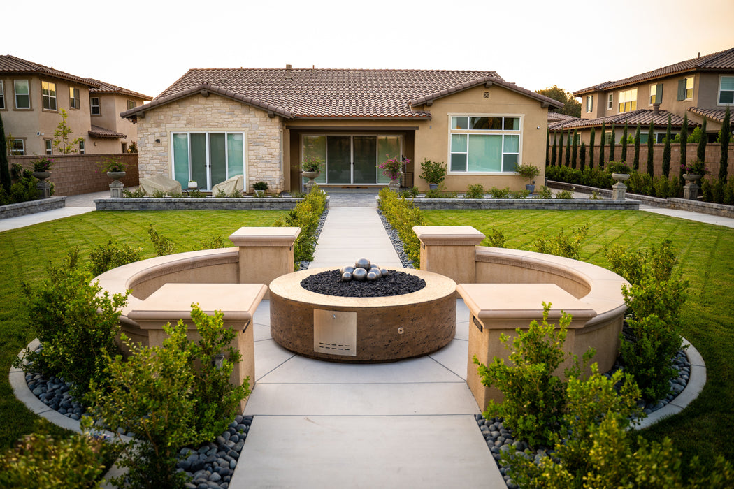 Elegant and modern Unity Round Fire Pit by The Outdoor Plus, finished in pewter powder-coated steel, providing a central gathering place in a landscaped backyard