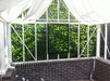 Interior view of the Victorian greenhouse showing white curtains for shade, with green foliage visible through the clear glass panels.