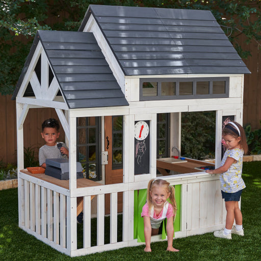 White wooden playhouse on a backyard with kids