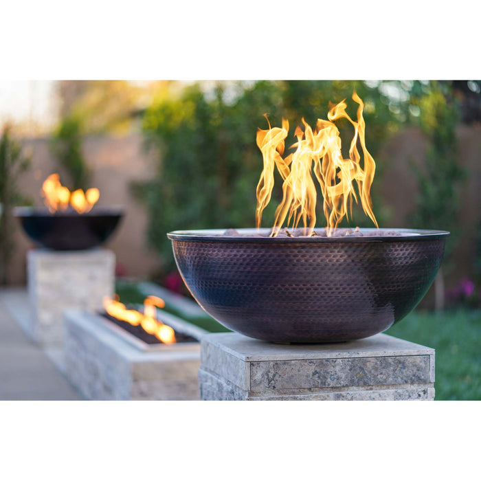 Lit 27" Round Sedona Hammered Copper Fire Bowl outdoors with other fire pits