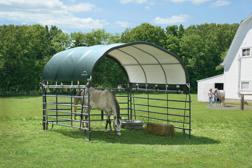 White horse standing in a ShelterLogic corral shelter with a green and white roof. The horse is eating grass and there is a bowl of water next to it.