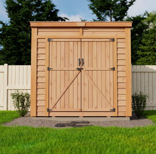 A wooden 8x4 GardenSaver with a single door, positioned on a lush green lawn beside a stone pathway, surrounded by tall green trees under a clear sky.