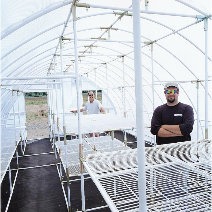 Two men inside the spacious Solexx Conservatory Deluxe greenhouse during setup, with empty plant shelves and the structure's sturdy frame visible