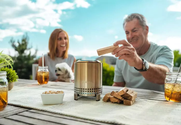 Man putting wood on Mesa stainless steel Tabletop Fire Pit.