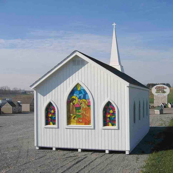 A playful representation of a chapel playhouse by Little Cottage Company, featuring vibrant stained glass windows, under a bright blue sky.