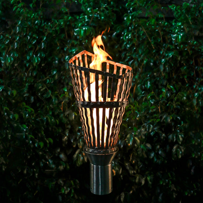 The Outdoor Plus Roman torch featuring a stainless steel design with original TOP torch base, ignited and set against lush greenery