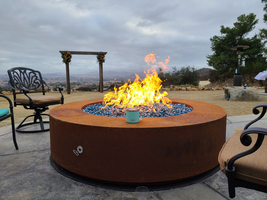 The Outdoor Plus Unity Round Fire Pit in pewter powder-coated steel, offering a stunning visual and heat source on a hilltop with expansive views.