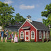 Children happily entering the Little Cottage Company Stratford Schoolhouse Playhouse in a lush garden setting.