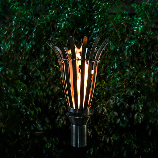 The Outdoor Plus Basket Torch with Original TOP Torch Base in stainless steel, showcasing a vibrant flame set against lush green foliage