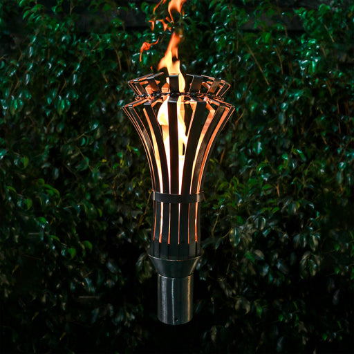 Elegant stainless steel Gothic Torch from The Outdoor Plus with Original TOP Torch Base, featuring a striking flame against a dense green backdrop