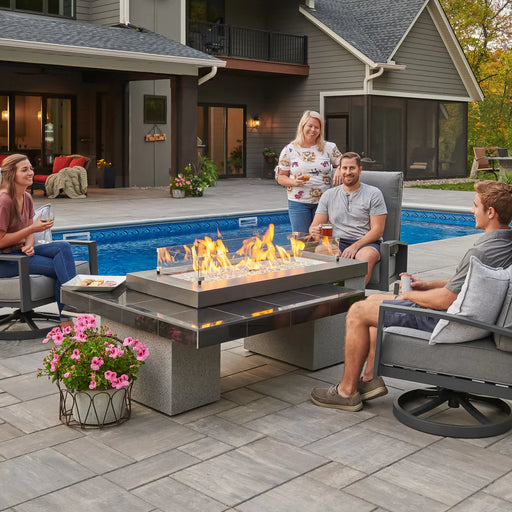 A family enjoys an outdoor gathering around the Fire Pit Table, beside a pool