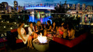 Friends gather around the warm glow of the Solus Decor Hemi Firebowl on an urban rooftop patio, creating an inviting atmosphere.