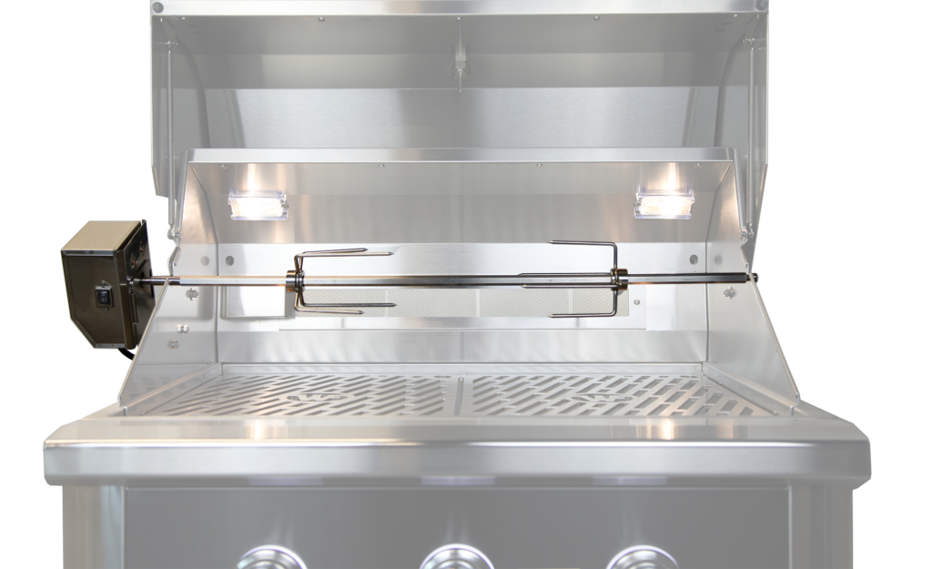 Wildfire Stainless steel rotisserie kit installed inside a grill, featuring a spit rod, motor attachment on the left, and two bright interior lights illuminating the cooking area.