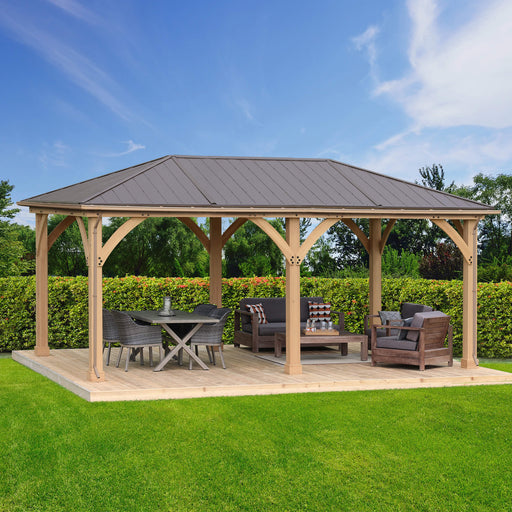  A spacious outdoor gazebo from Yardistry's Meridian series, featuring a functional rain gutter kit along its metal roof, set in a lush garden for an ideal outdoor retreat, complete with comfortable patio furniture.