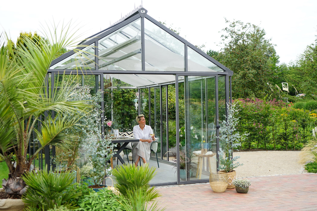 A tranquil exaco greenhouse setting with a woman in relaxed attire enjoying a beverage at a dining table.