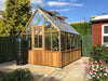 Alton Cheltenham Victorian Greenhouse set against a green garden with dark fencing and flowers.