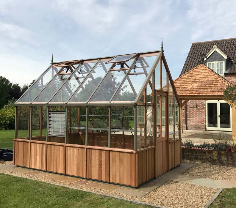 Alton Cheltenham Greenhouse situated on a paved garden area next to a house.