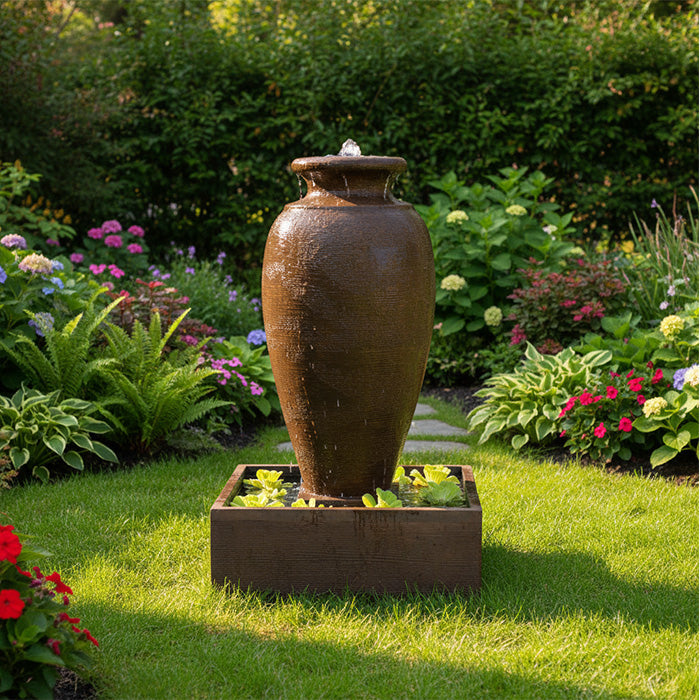 Amphora patio water feature with textured urn design and square base, placed on stone pavers near flower display.