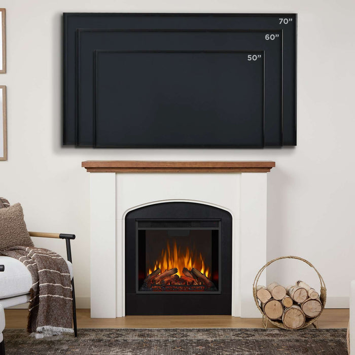 Real Flame Anika white electric fireplace with black surround in living room beneath wall-mounted TV showing 50", 60", and 70" size comparisons, with log basket and armchair