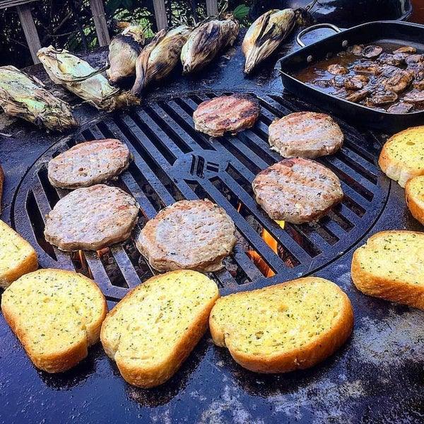 Arteflame Black Label 30" grill in use, cooking burgers and toasting garlic bread, exemplifying its outdoor entertainment capabilities.