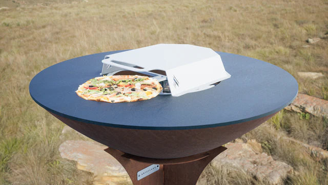 Arteflame pizza oven with a pizza on the cooking surface, and the oven lid propped open.